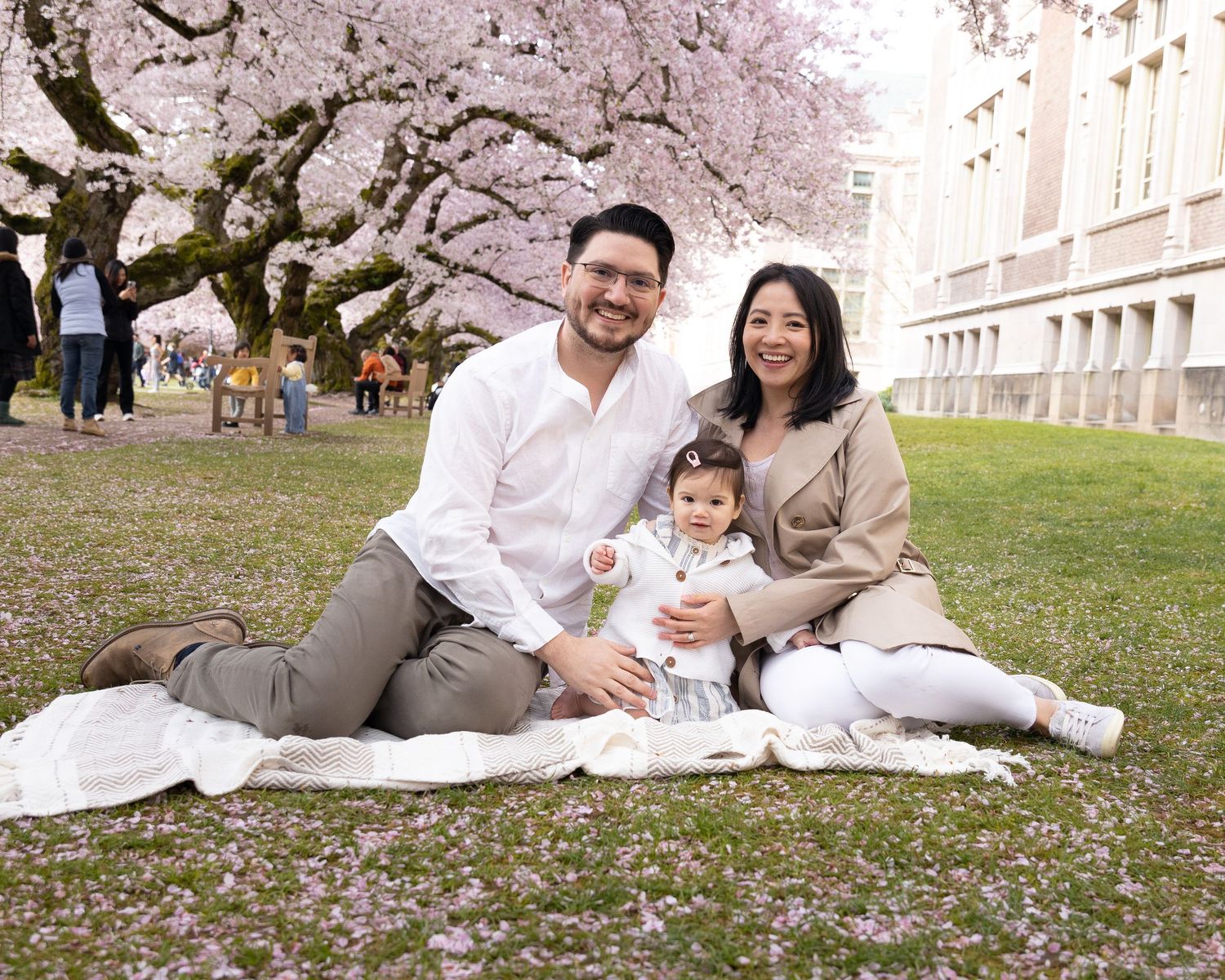 Family enjoying a picnic under blooming cherry blossom trees on a spring day.