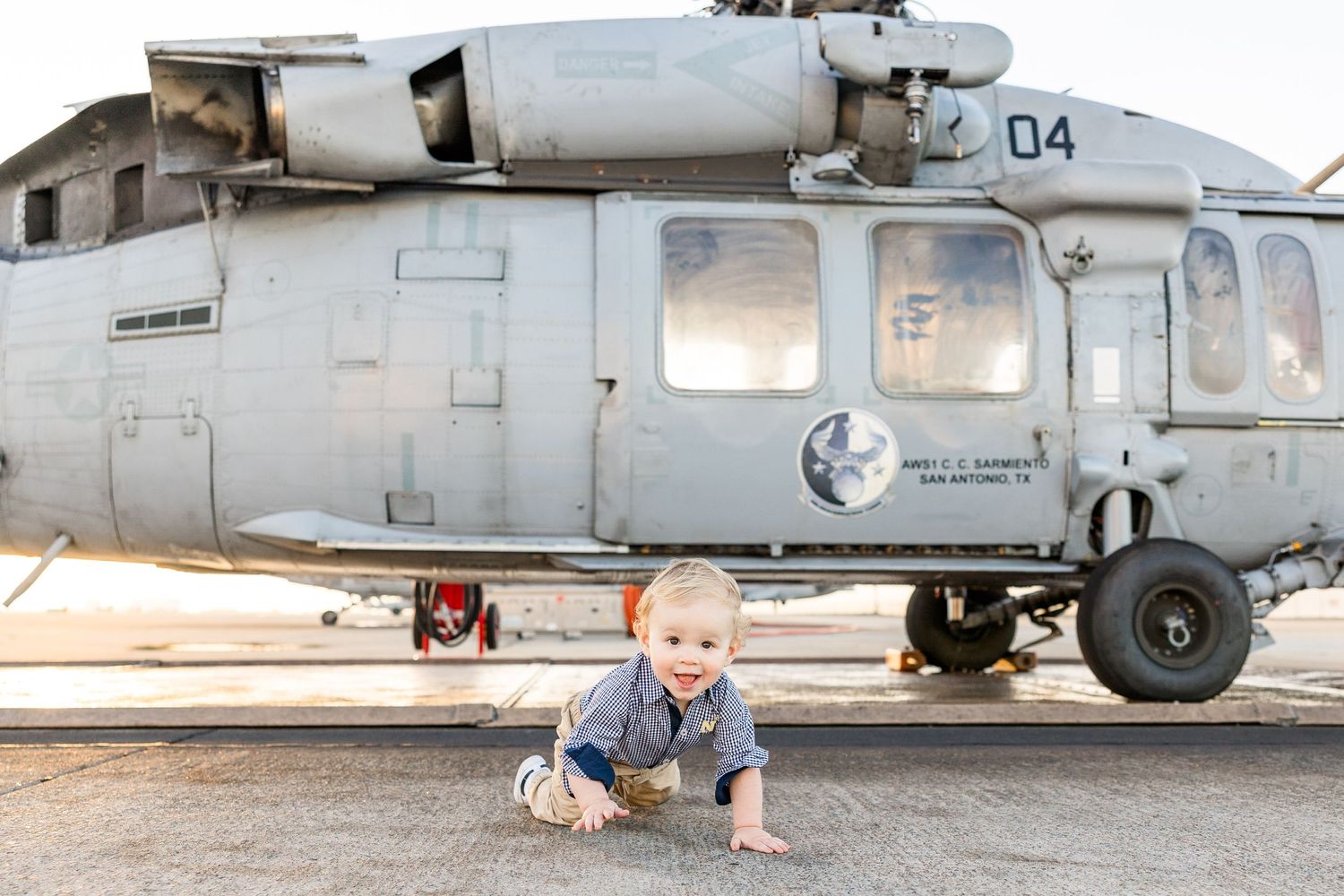 Small child crawling on ground in front of large military helicopter.