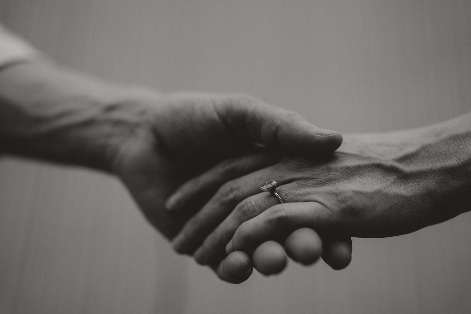 Black and white close-up of hands holding with wedding ring detail.