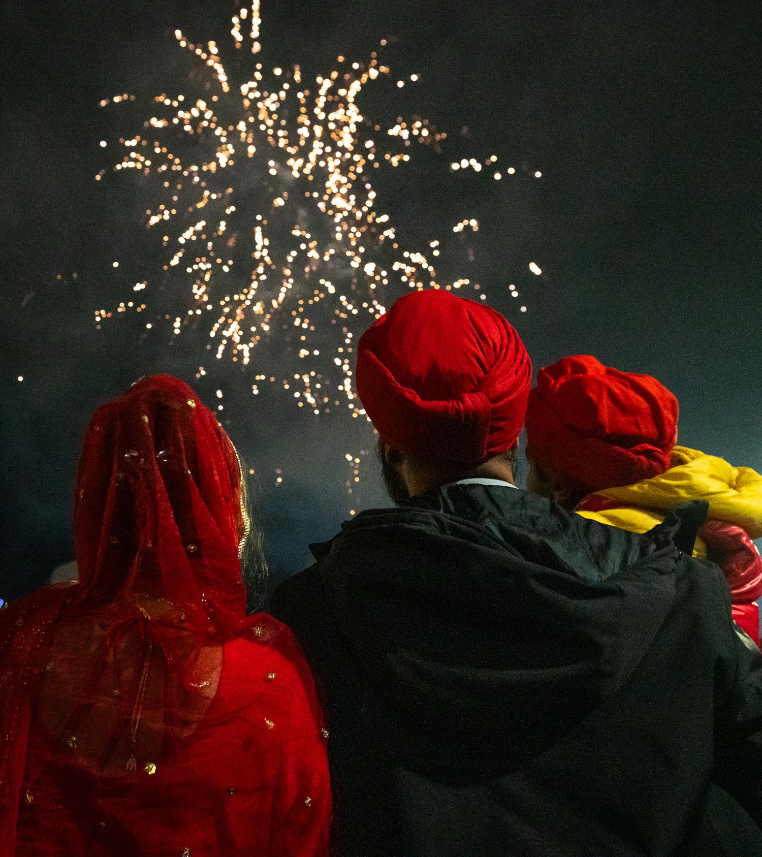 People in red attire watch fireworks light up the night sky during a celebration.