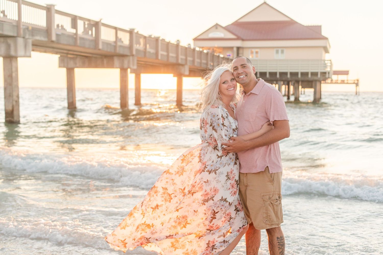 Couple embracing by wooden pier at beach during golden hour.