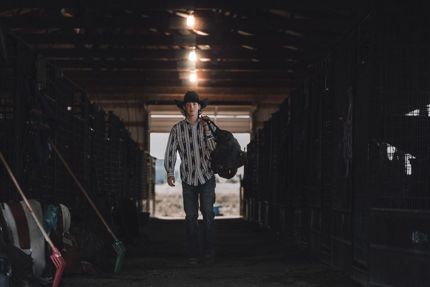 Silhouetted figure standing in a dark barn doorway with sunlight streaming in behind.
