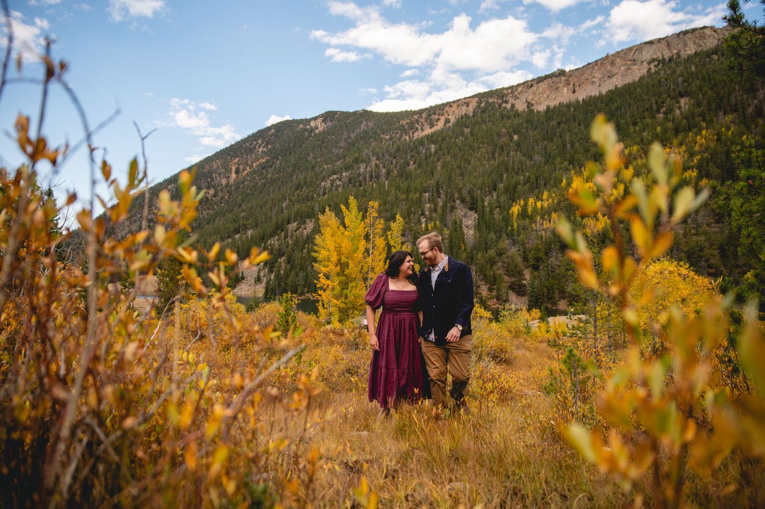 Couple poses against mountainous backdrop with golden autumn foliage.