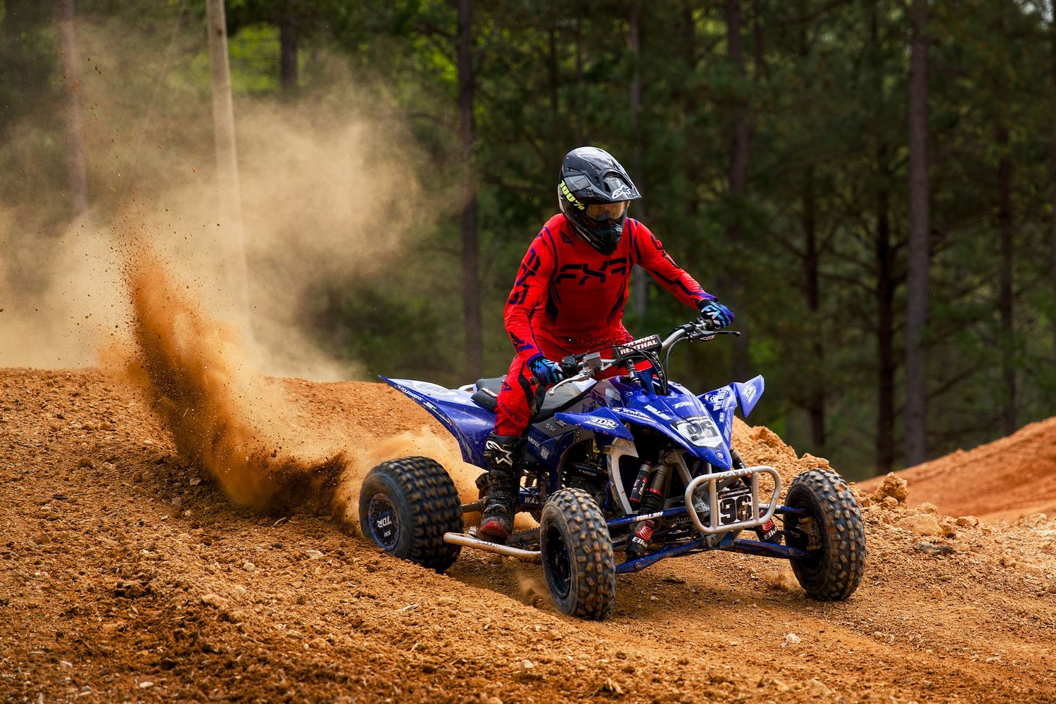 Dirt bike and ATV riders kicking up dust clouds while racing through an off-road dirt track.