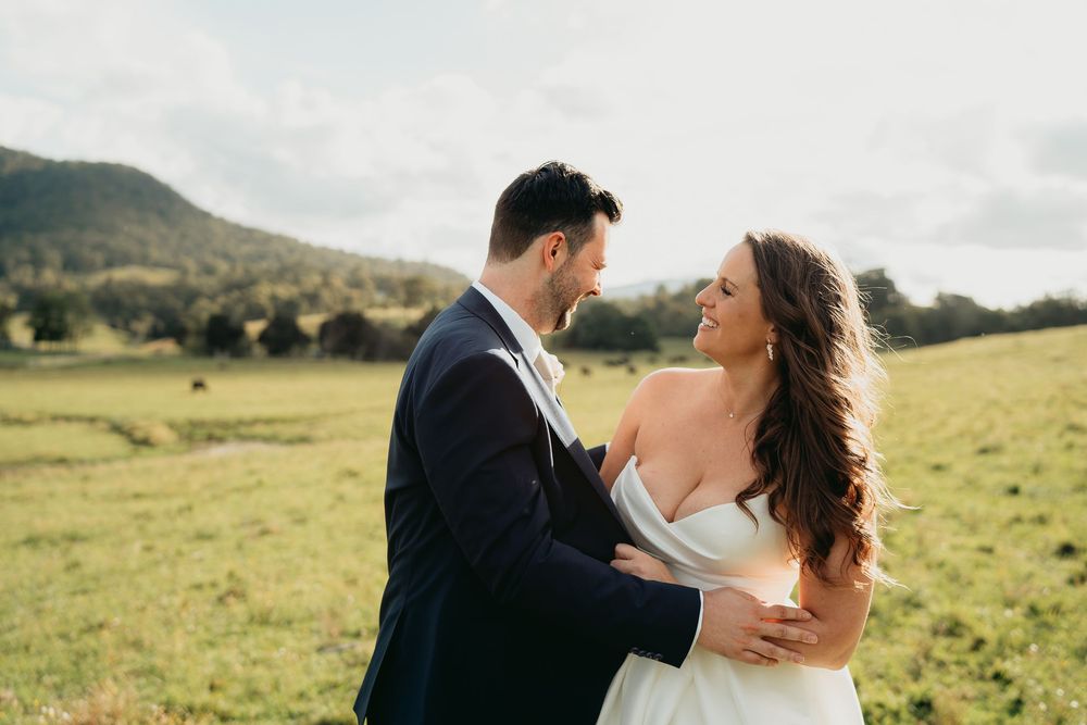 Couple in formal wedding attire embrace lovingly in a scenic mountain meadow with rolling hills in the background.