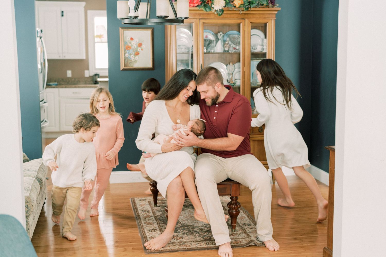 Family gathering in living room with children playing while parents hold baby.
