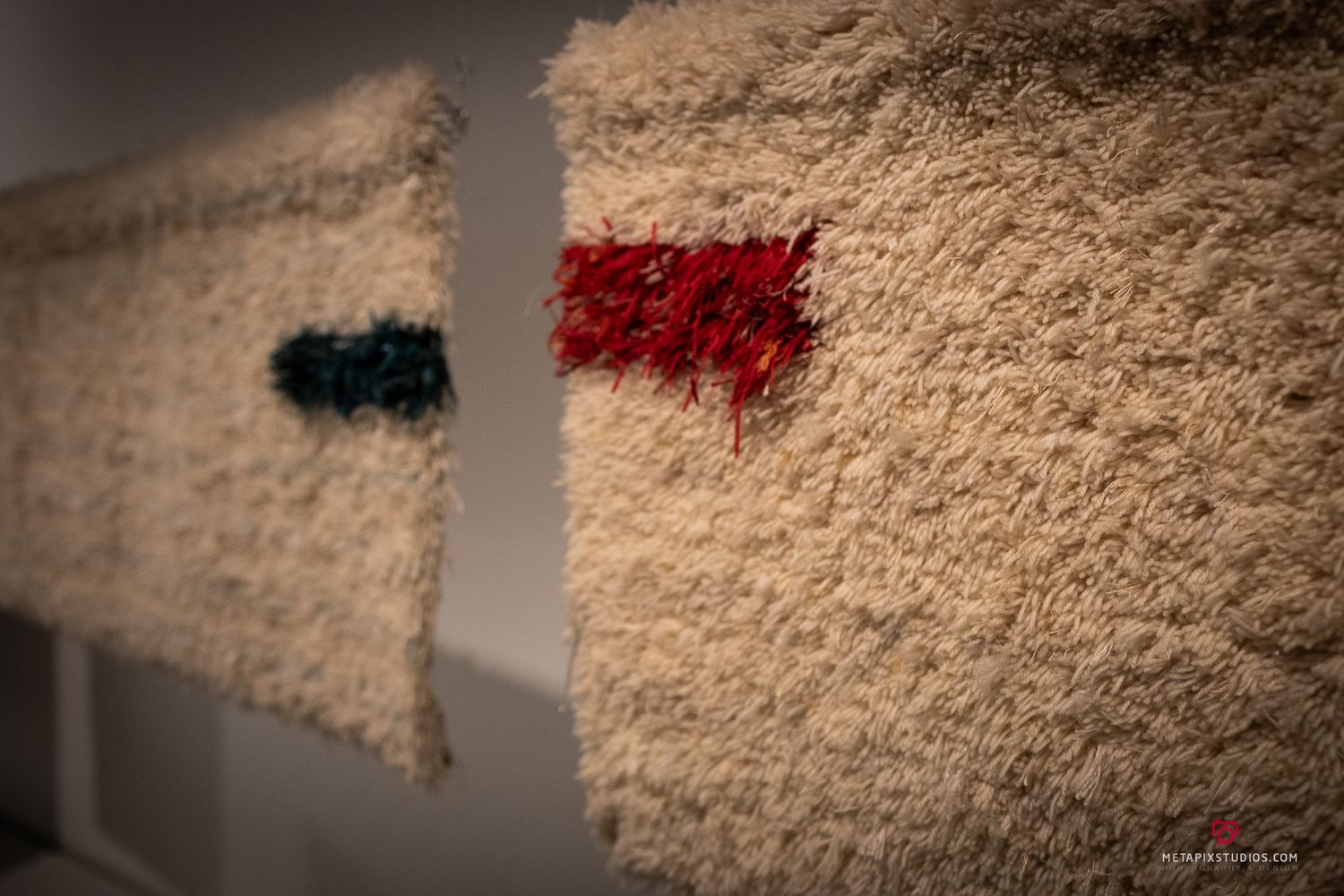 Two textured wool fabric samples mounted on a white wall with small red and teal woven accent patches.
