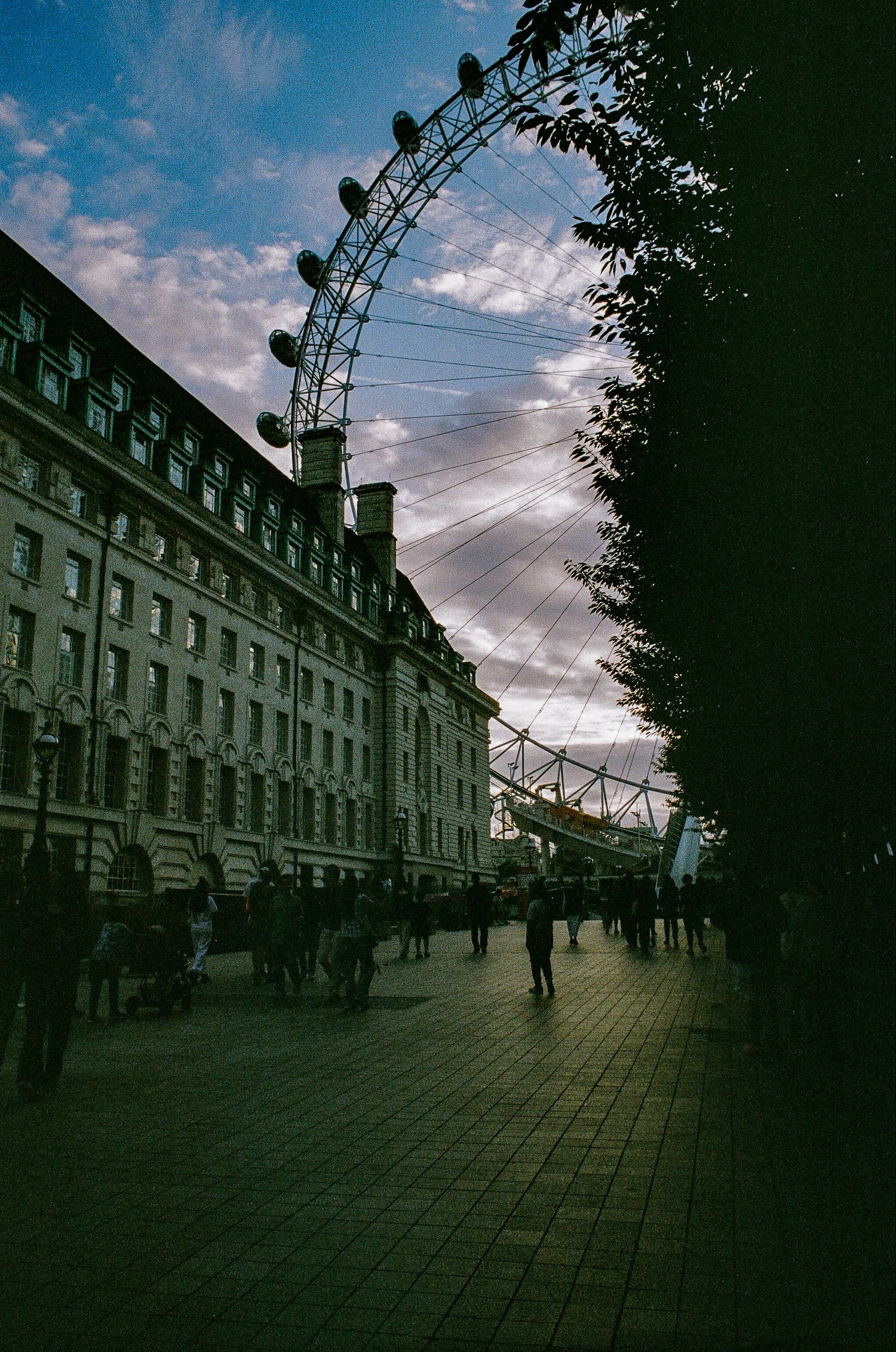 The London Eye Ferris wheel against a dramatic sunset sky with historic buildings along South Bank.