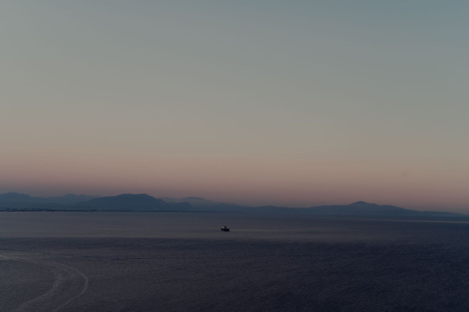 A minimalist landscape showing mountains in soft evening light with hazy atmosphere.
