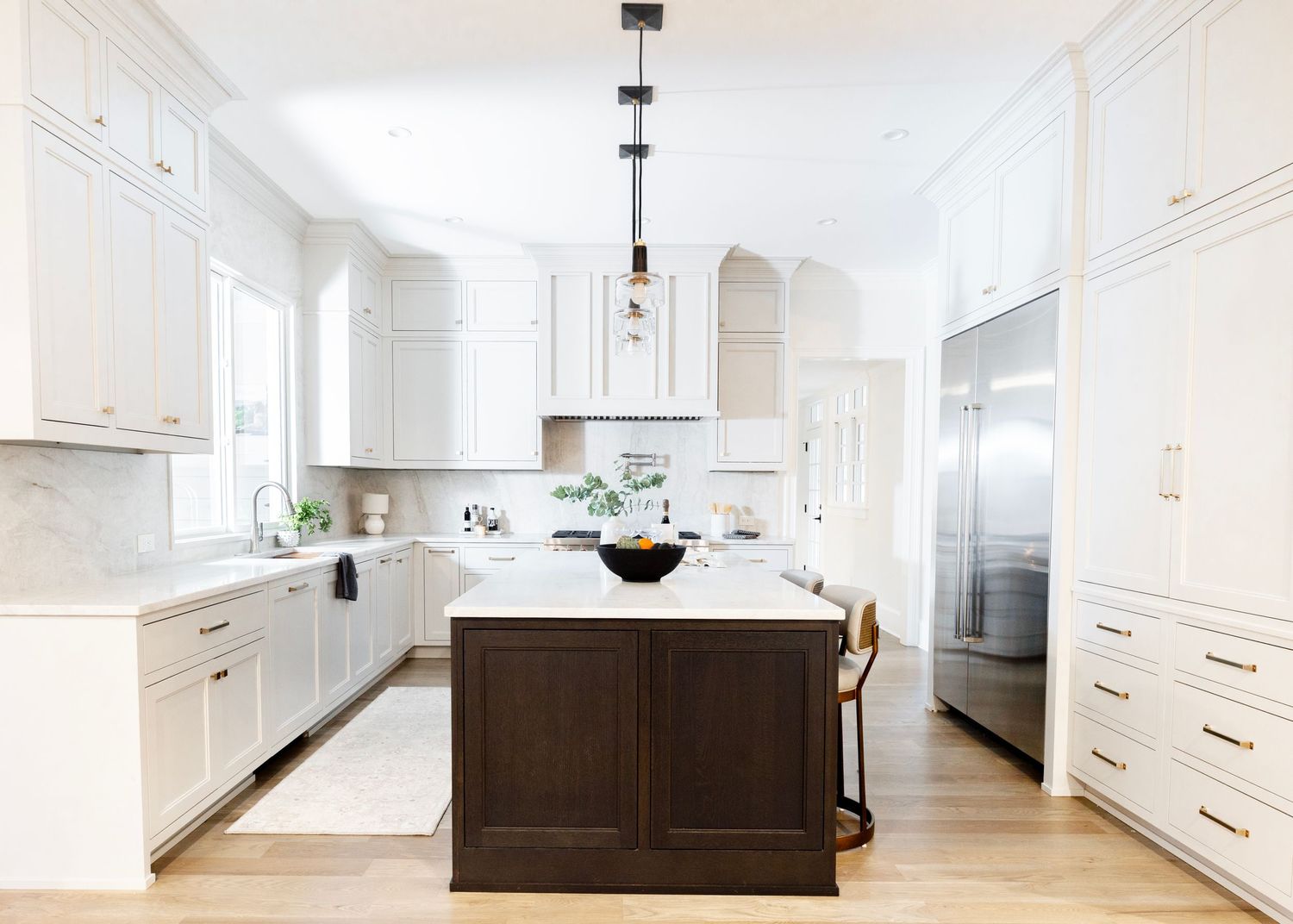 Bright white modern kitchen with dark wood island, white marble countertops, pendant lights and hardwood floors.