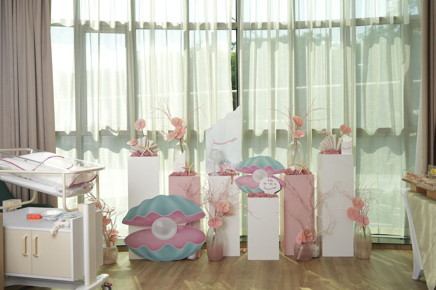Pink and white party setup with floral decorations near sheer curtains.