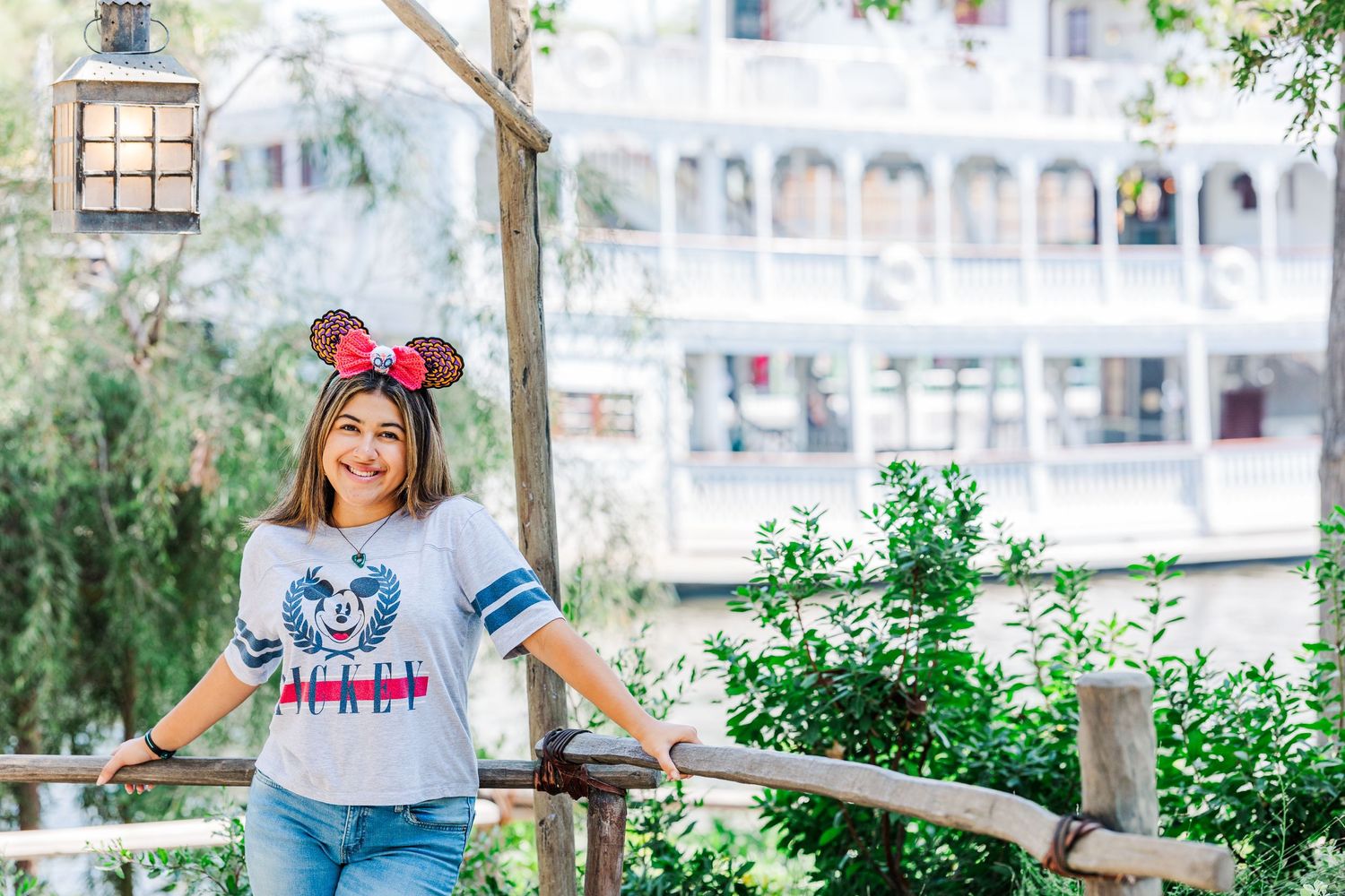 Disney fan wearing Mickey ears poses at theme park with white building in background.
