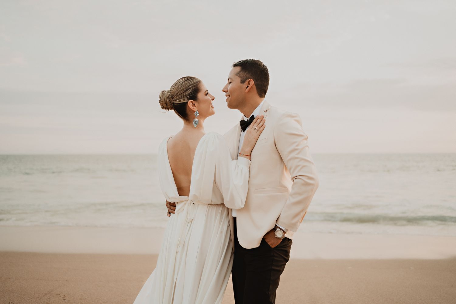 Elegant couple looking at each other with smiles, hand on waist and chest, with ocean backdrop
