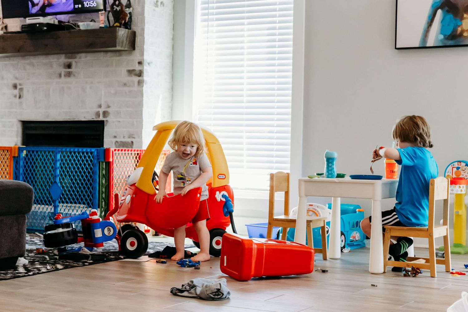 Children play with toys in a bright living room featuring a small red car and colorful furniture.