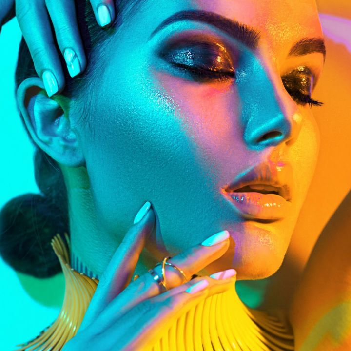 Creative beauty portrait with dramatic blue and orange lighting on a model wearing yellow and showing vibrant makeup.