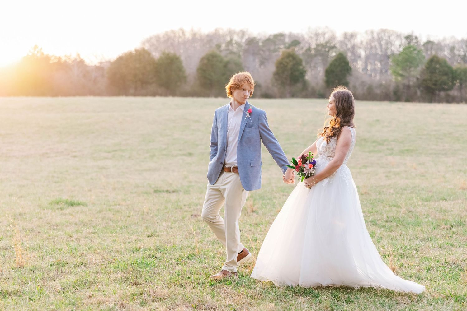 A dreamy golden hour wedding photo of a couple dancing together in an open field.