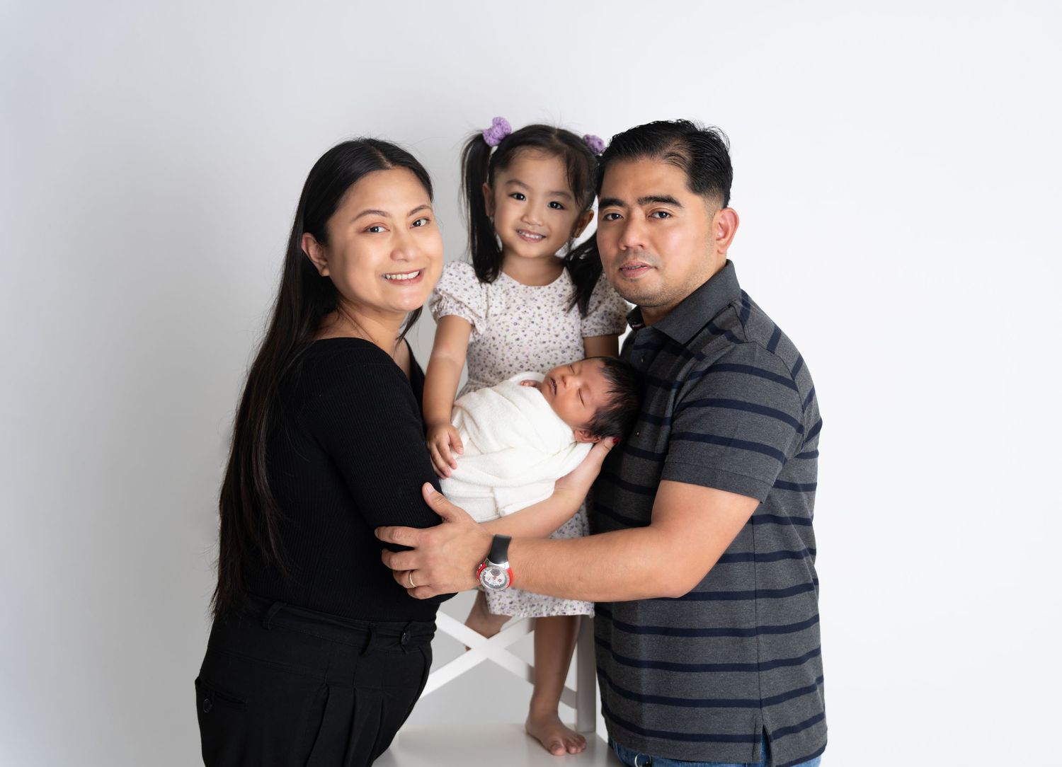 Three family members wearing casual clothing pose together against a white studio background.