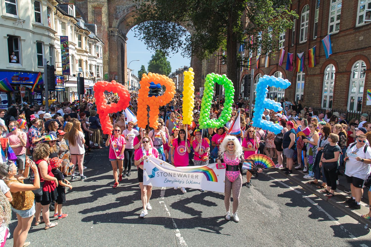 Colorful balloon letters spelling PRIDE carried through crowded street during pride parade celebration.