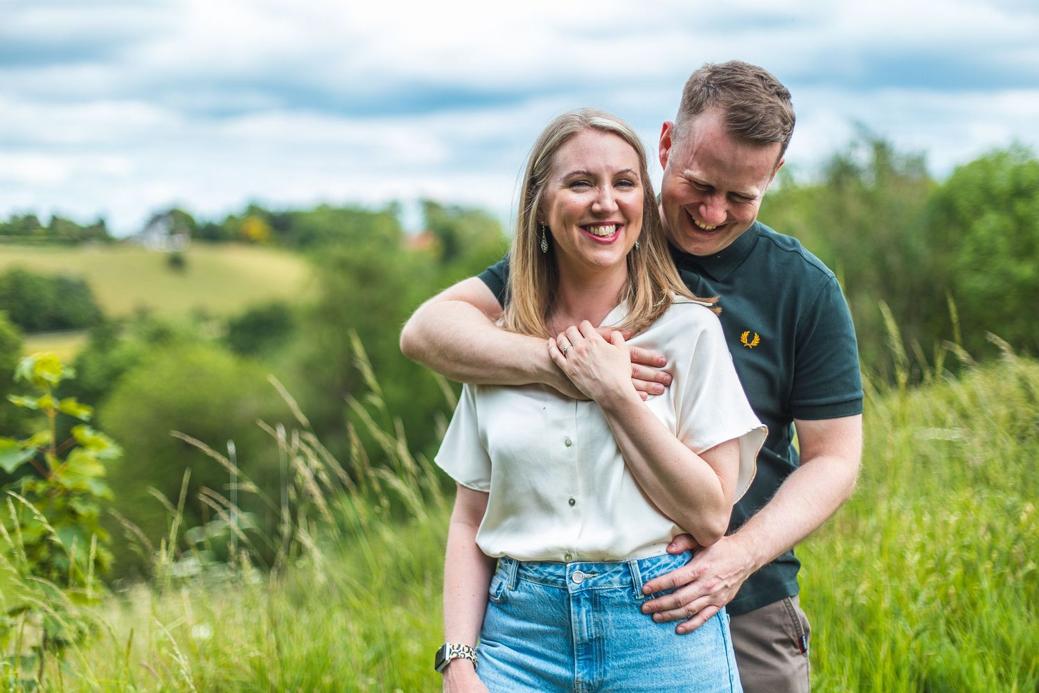 Happy couple embraces and laughs together in a sunny green meadow on a summer afternoon.