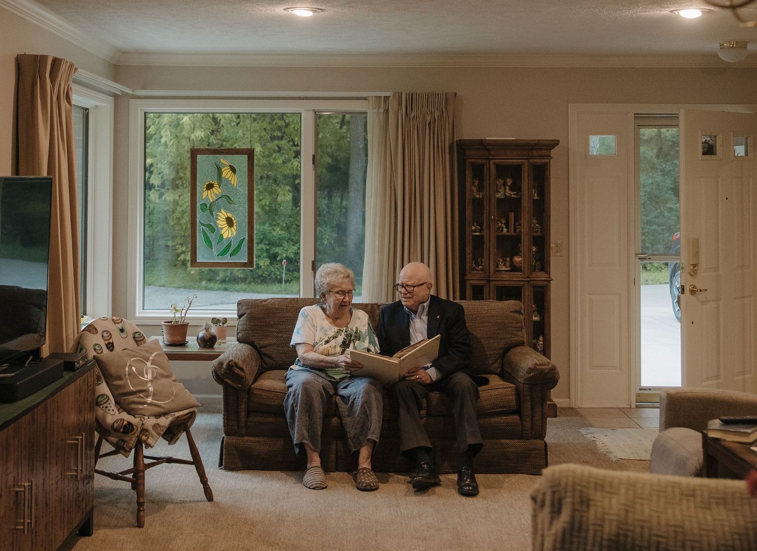 An elderly couple sits close together on a couch, sharing a candid moment of laughter and companionship.