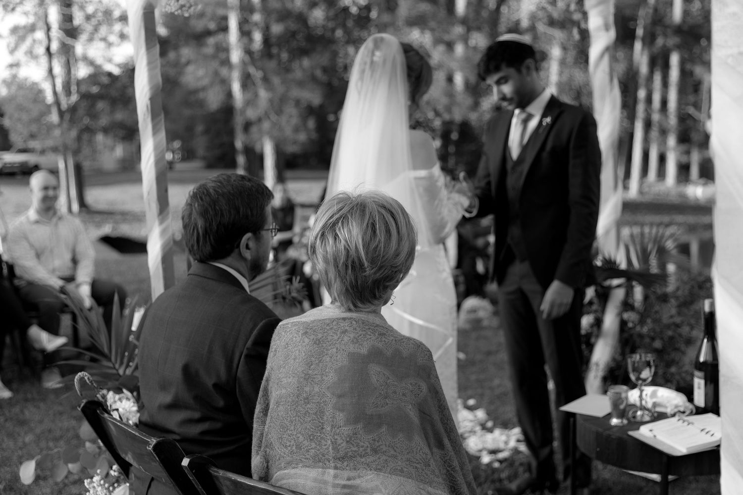 Vintage black and white photo of an outdoor wedding ceremony in a wooded setting.