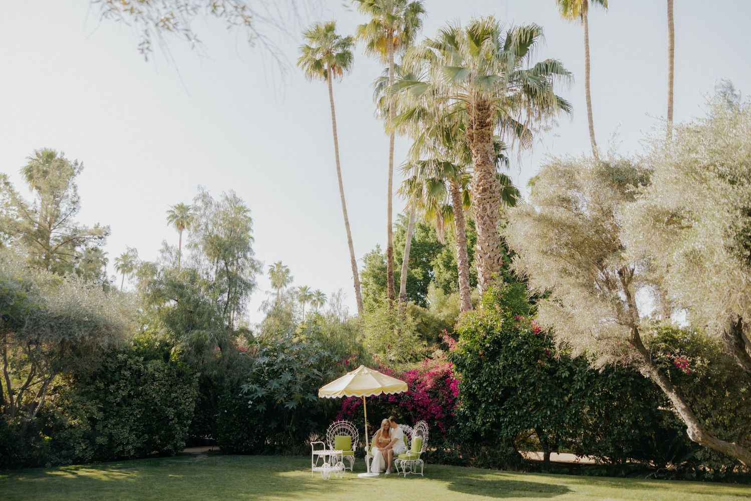 Palm trees and umbrella shade a garden party setting.