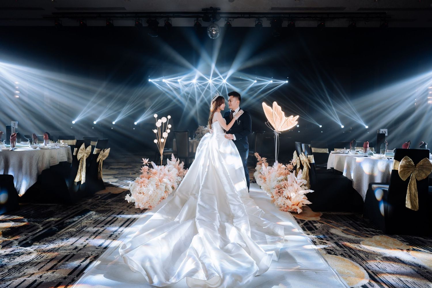 Wedding couple under dramatic spotlight beams in elegant ballroom reception.