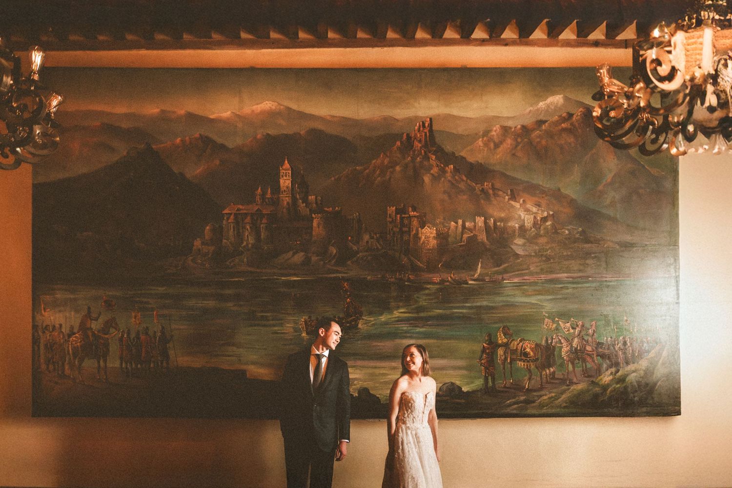 Wedding couple standing in front of large vintage landscape paintings in a grand room.