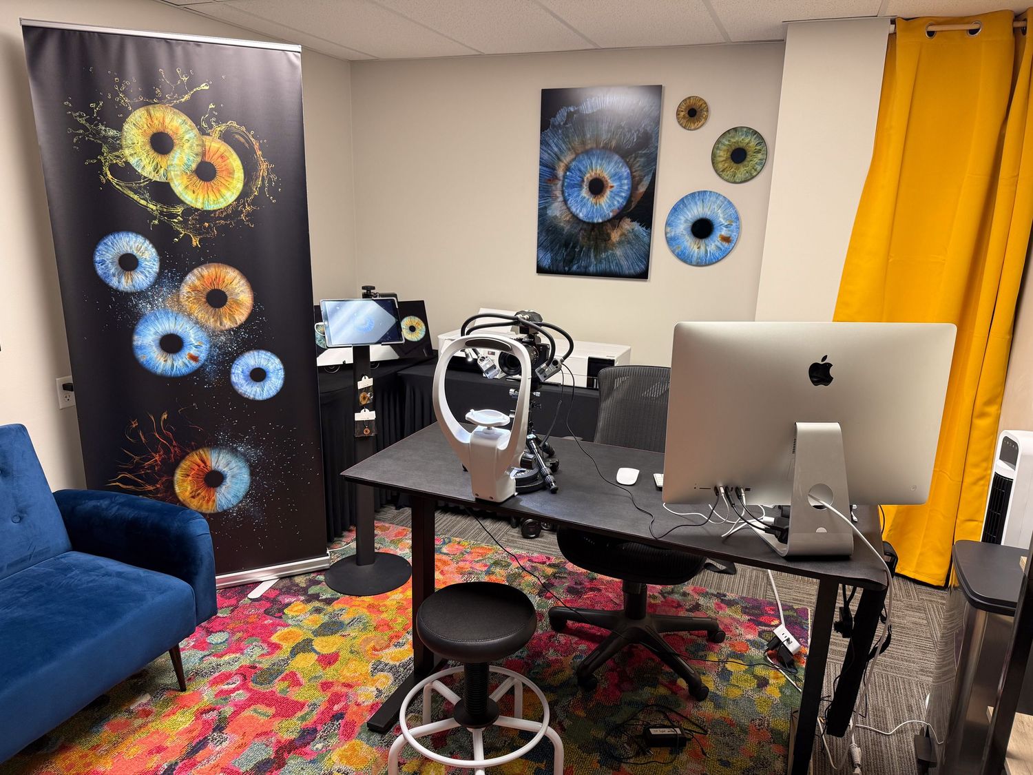 Modern home office setup with black desk, colorful carpet, blue couch, and wall art featuring circular donut designs.