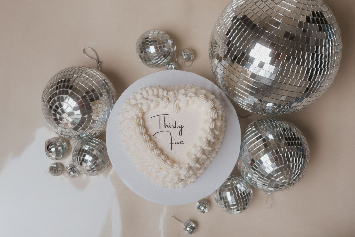 Shiny disco balls scattered around white ceramic place cards on a light neutral surface.