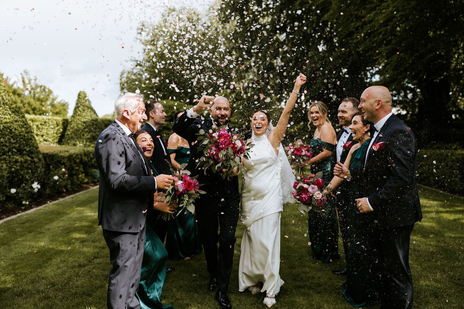 Wedding guests throw confetti in joyful celebration at an outdoor garden ceremony.