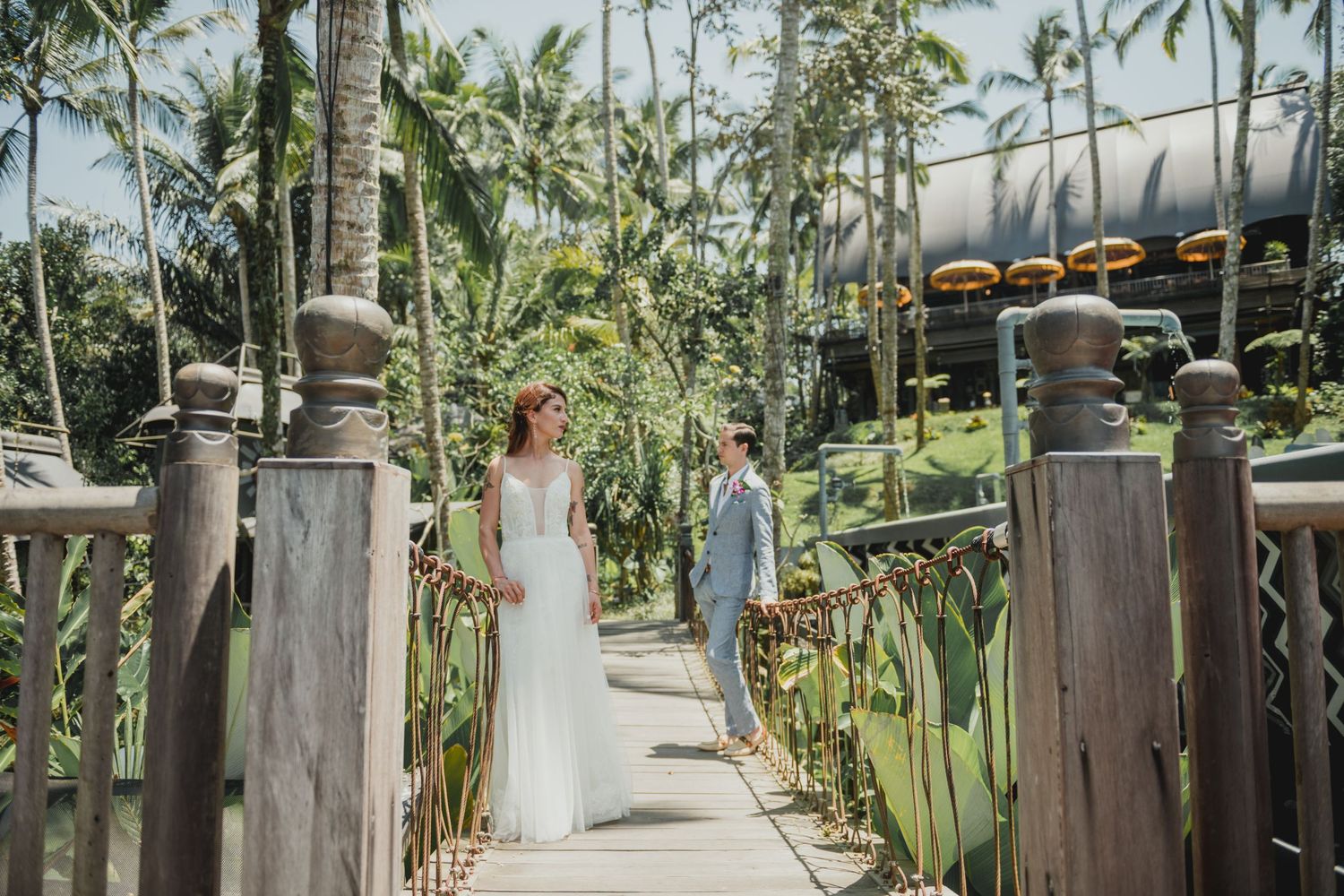 A couple walks through lush tropical greenery with palm trees framing the scene.