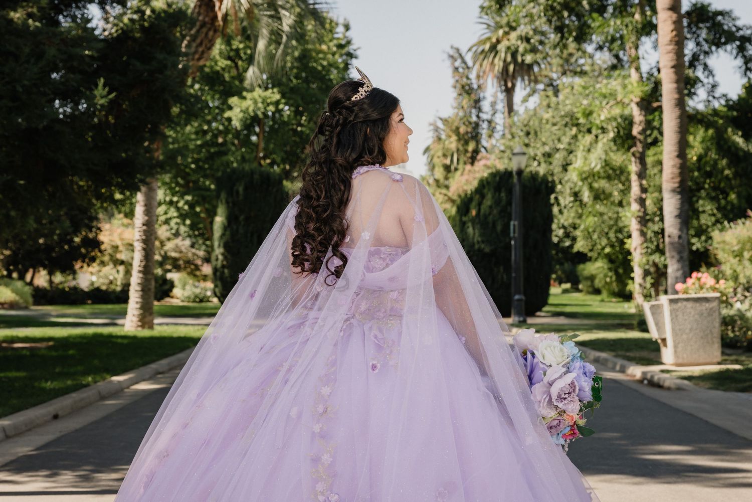 A quinceanera in a flowing champagne-colored ballgown stands on a gravel path at sunset for Bella Vista Farms quince celebration