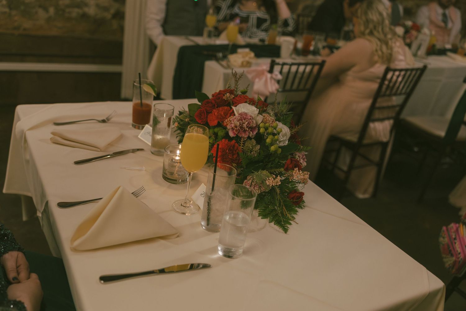 Elegant wedding reception table settings with chiavari chairs, white linens, and floral centerpieces in a banquet hall.
