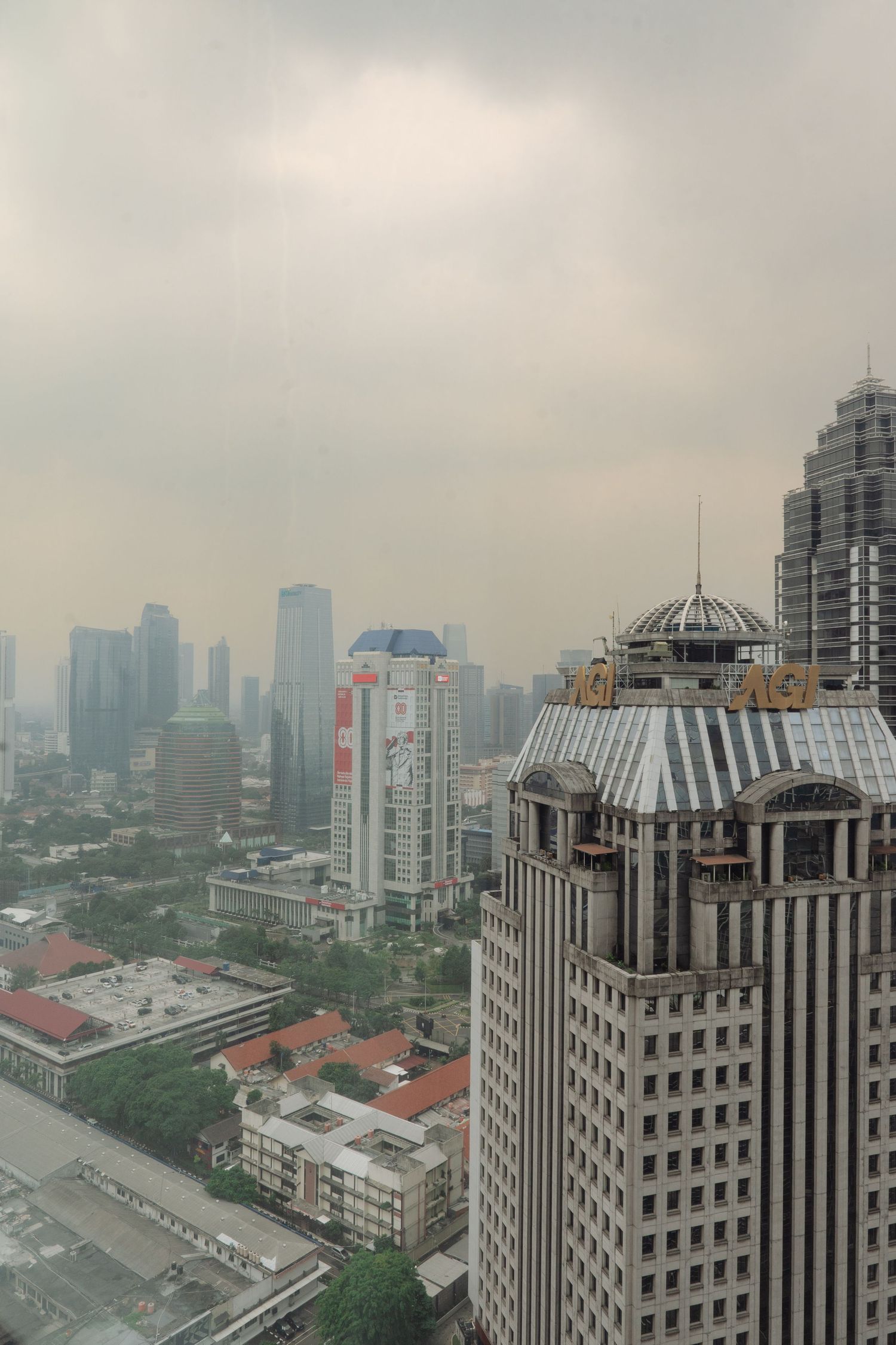 Hazy cityscape aerial view of Jakarta skyline with skyscrapers and overcast sky on a smoggy day.