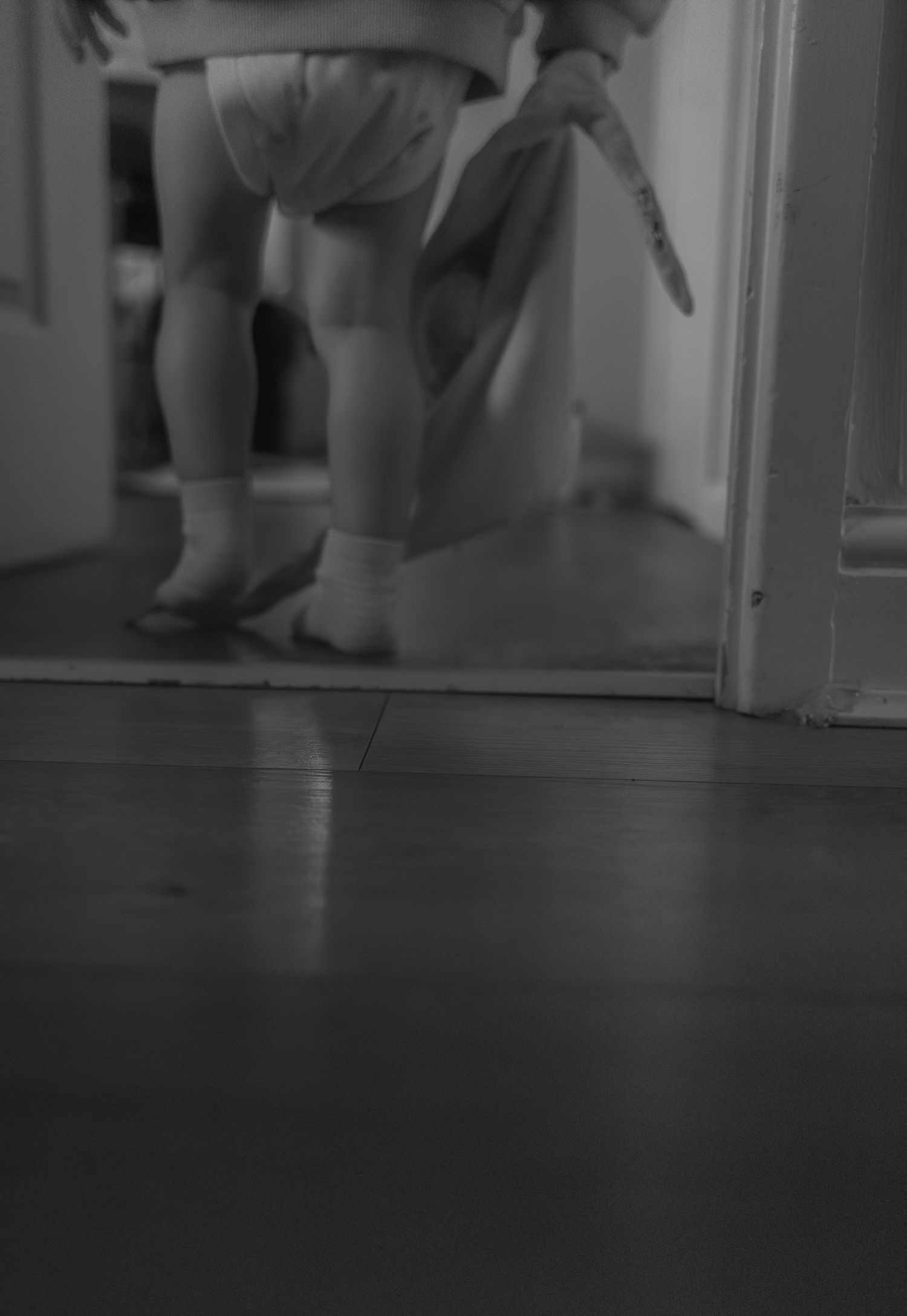 A black and white image shows feet and legs walking on a dark floor in an interior space.