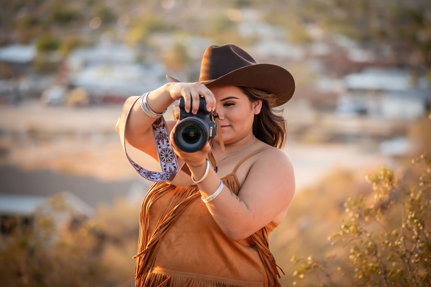 Professional photographer in a brown dress takes photos during golden hour in a wildflower meadow.