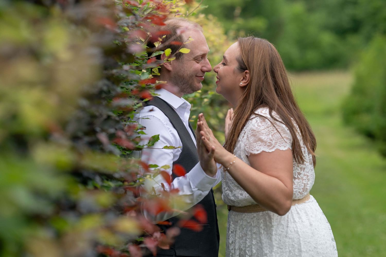 A couple in a garden shares a joyful moment while holding red berries from a nearby bush.