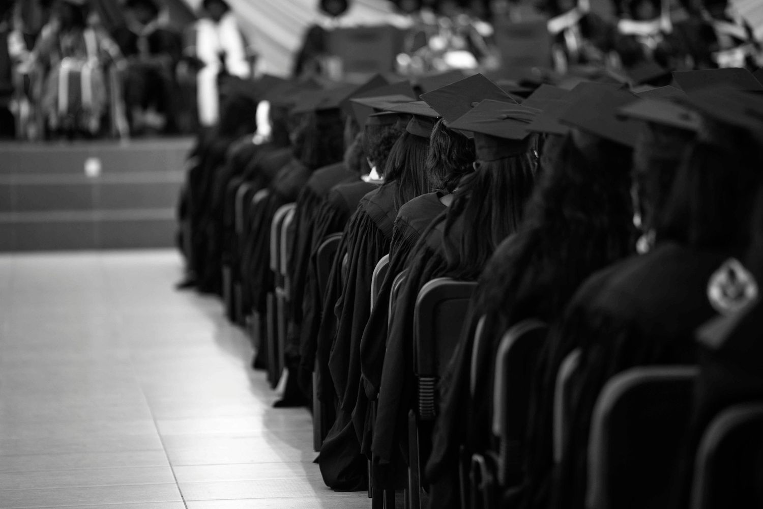 A crowd of people wearing black graduation caps and gowns stand in rows during a commencement ceremony.