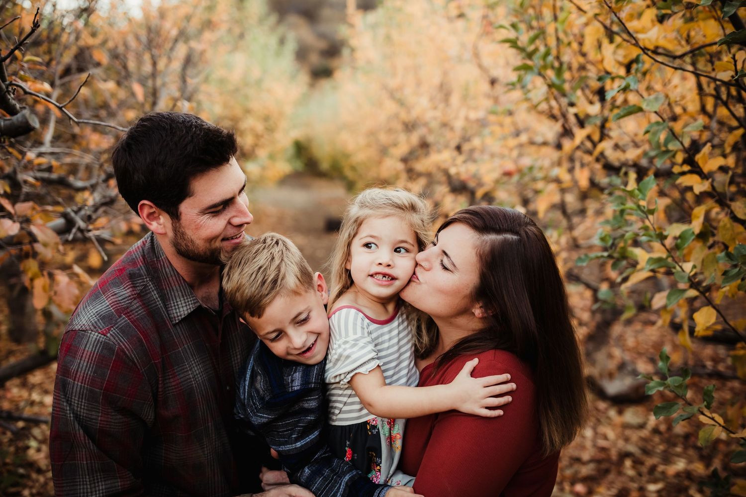 A family shares tender moments together during a fall photoshoot with golden autumn leaves in the background.