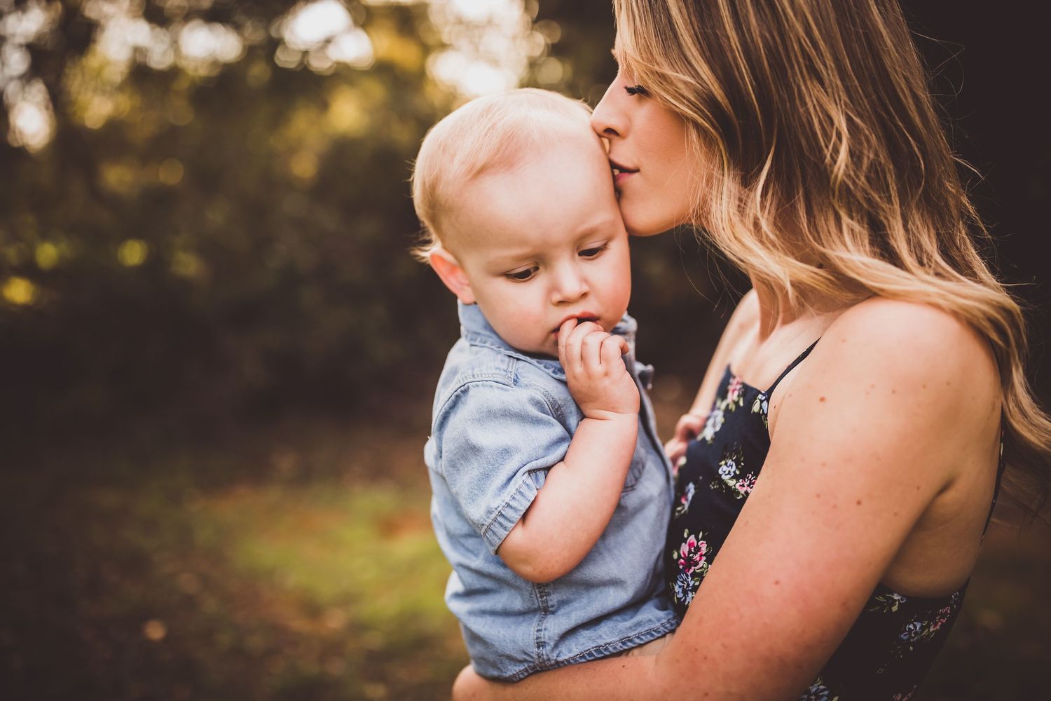 A tender moment between parent and baby in a light blue outfit against a golden sunset background in nature.
