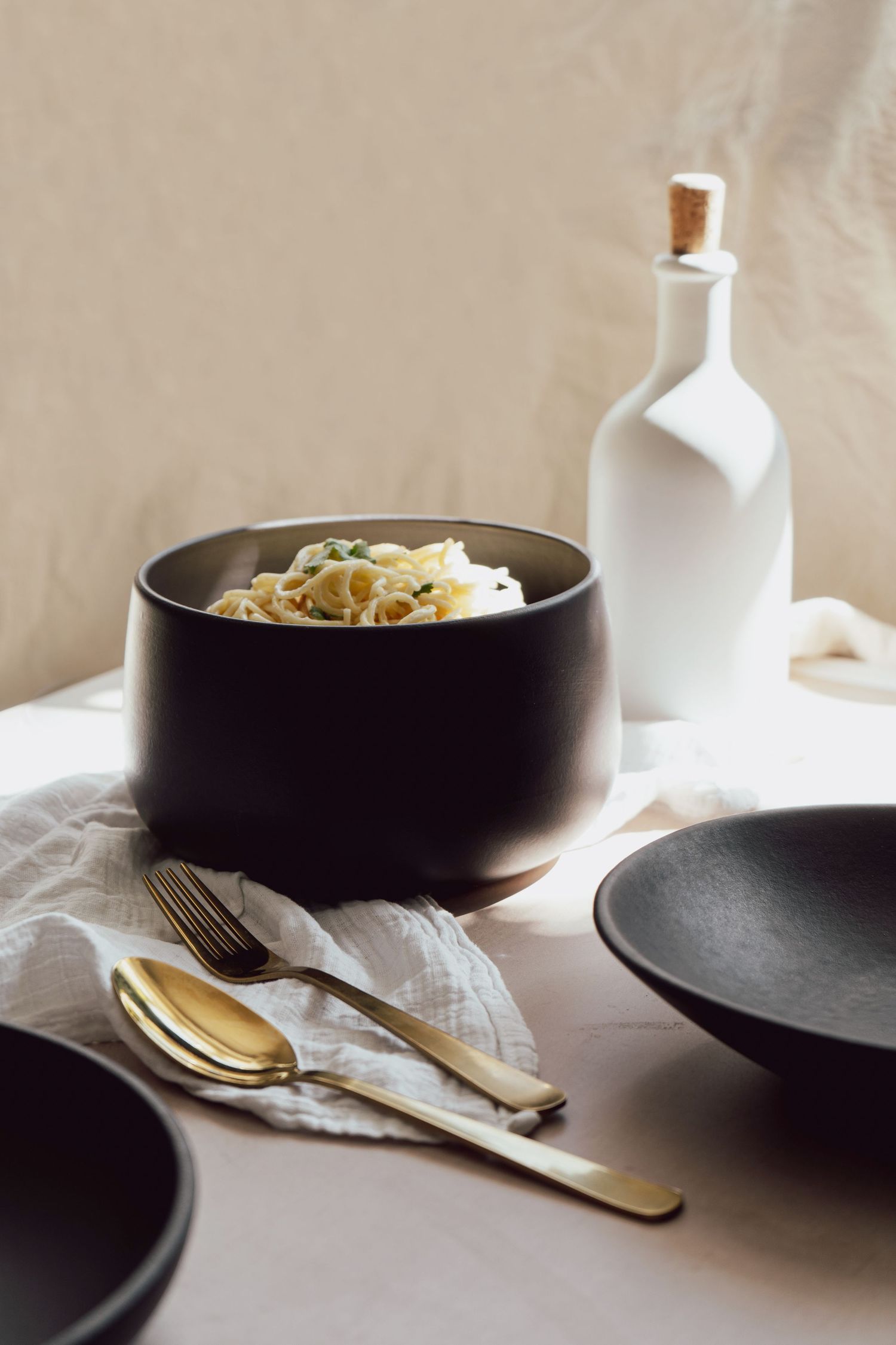 Contemporary natural light product photo of spaghetti in black bowl, black and white tableware in direct sunlight