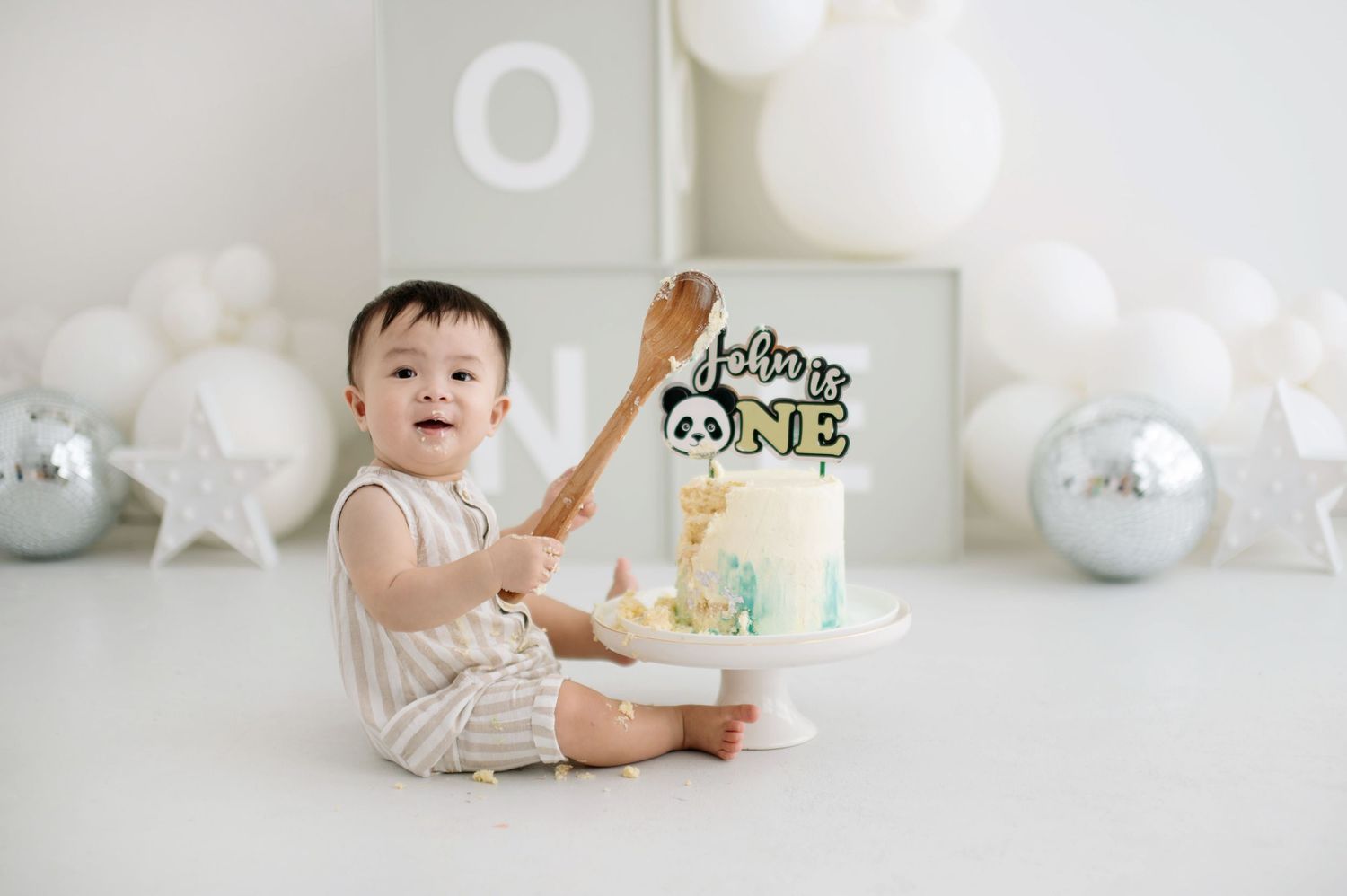A series of cake smash photos showing a one year old celebrating with white and silver party decorations and balloons.