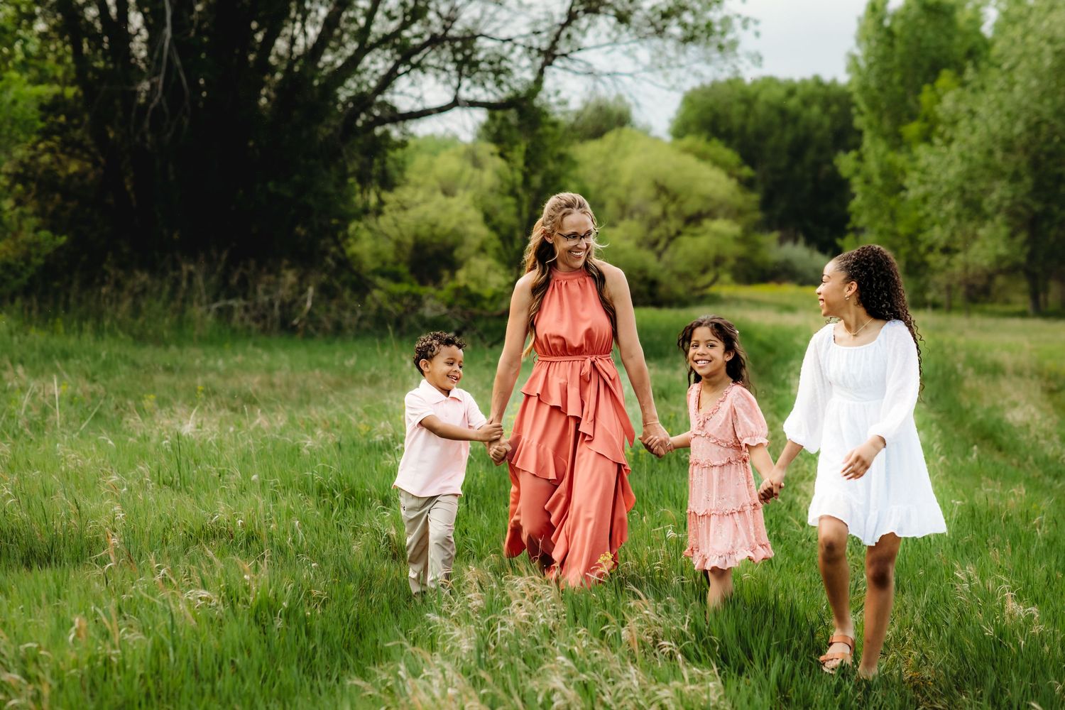 A group in coral and white dresses walks together through a lush green meadow on a sunny summer day.