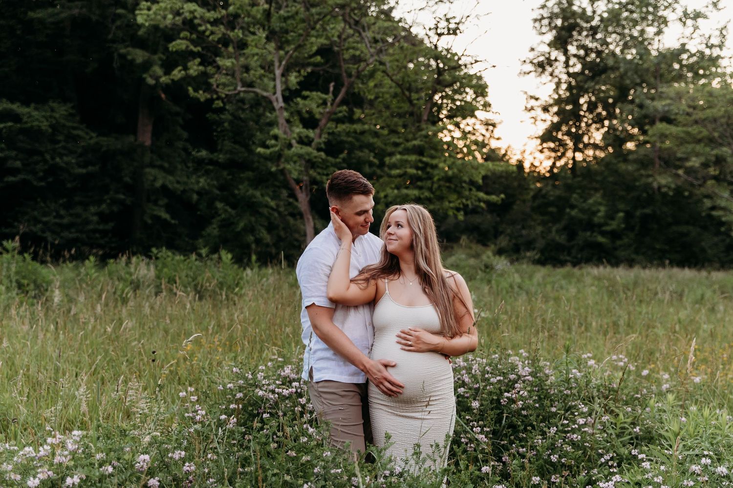 A romantic couple embraces in a sunlit meadow filled with wildflowers during a summer evening photoshoot.