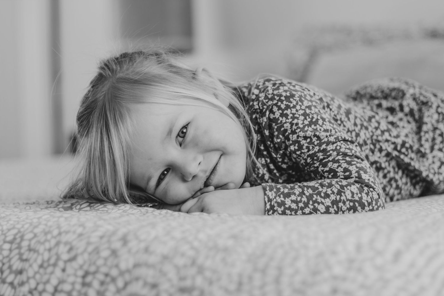 A child in a white shirt rests their head on their hands while lying down on a gray couch | Kids Birthday Photo Sessions