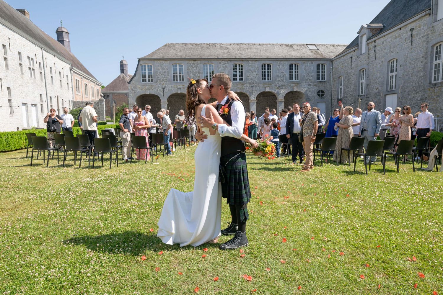 A couple dances on a lawn during an outdoor wedding celebration at a historic stone building with arched colonnade.