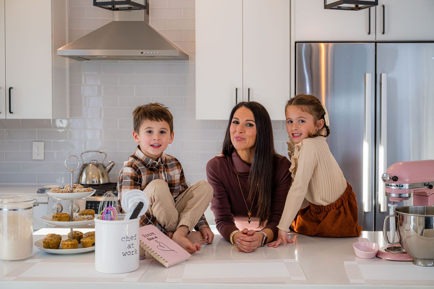 A group gathers around a modern white kitchen island enjoying snacks and conversation in a bright contemporary space.