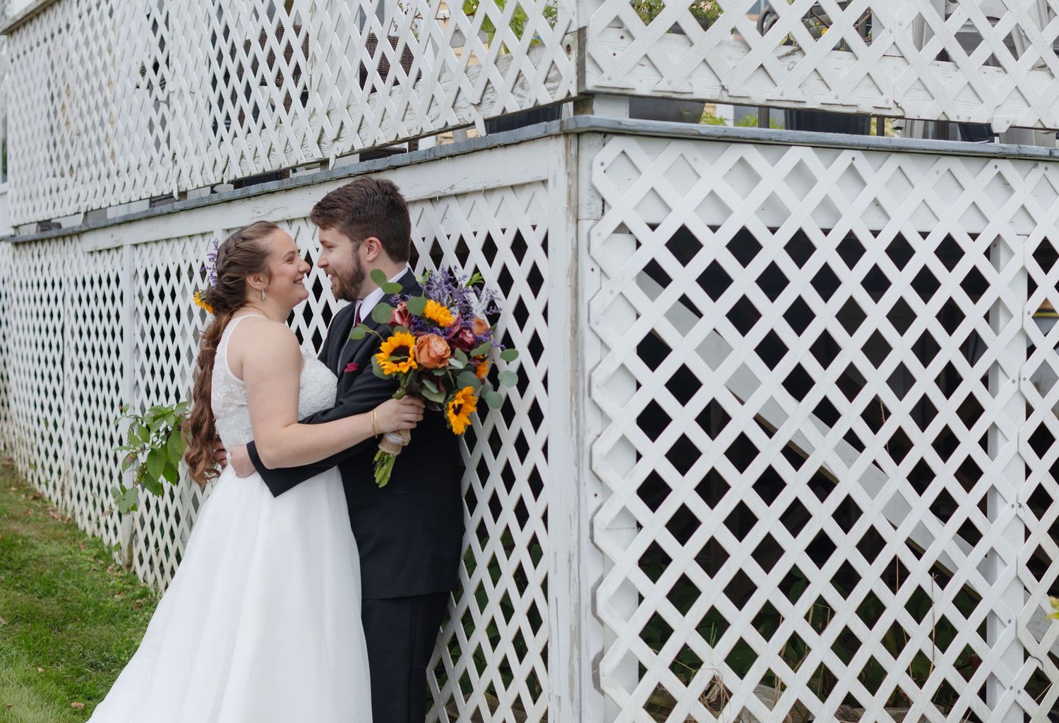 A couple shares an intimate moment in front of a white lattice fence during their autumn wedding ceremony at Westbrook Inn Derry NH
