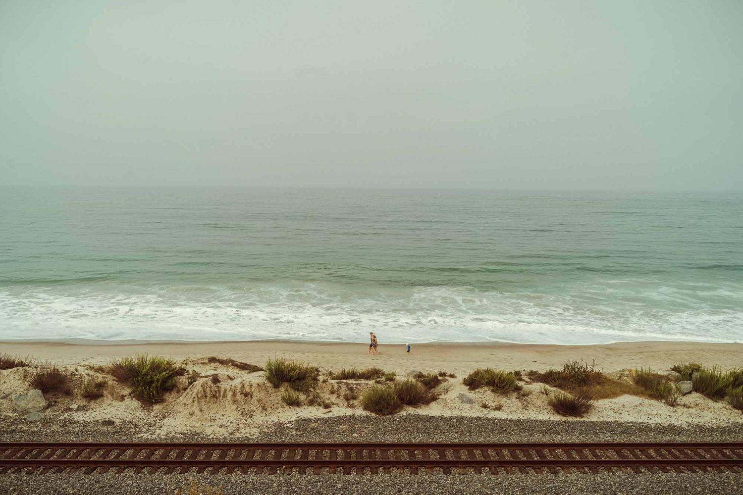 A series of coastal landscape photos showing ocean waves, train tracks, and misty beach scenes in muted teal tones.
